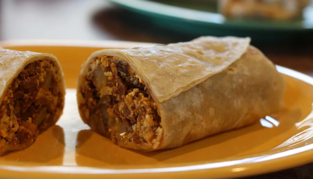 Halved breakfast burrito showing eggs, potatoes, and seasoned meat filling.