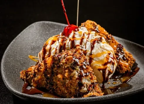 Fried ice cream with vanilla scoops, chocolate, caramel, and a red cherry.