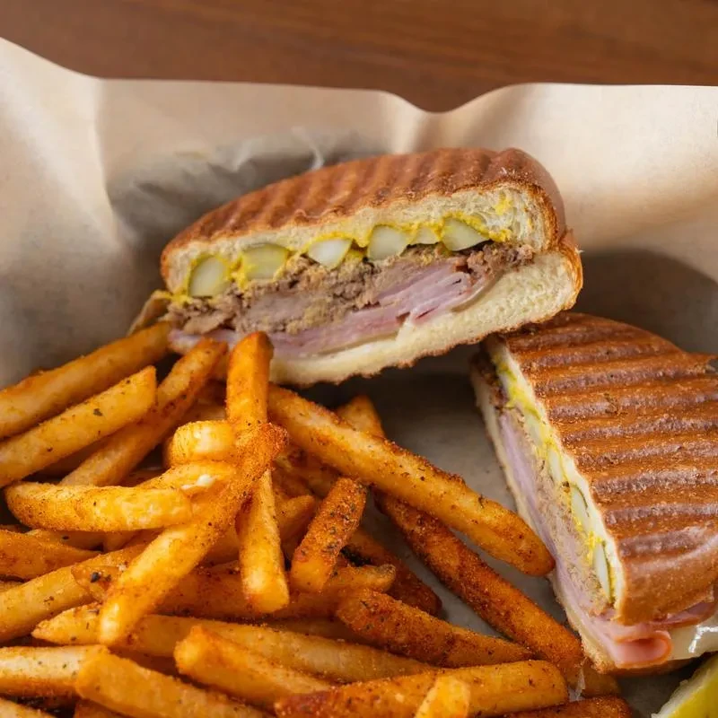 Grilled Cuban sandwich cut in half, with seasoned french fries.