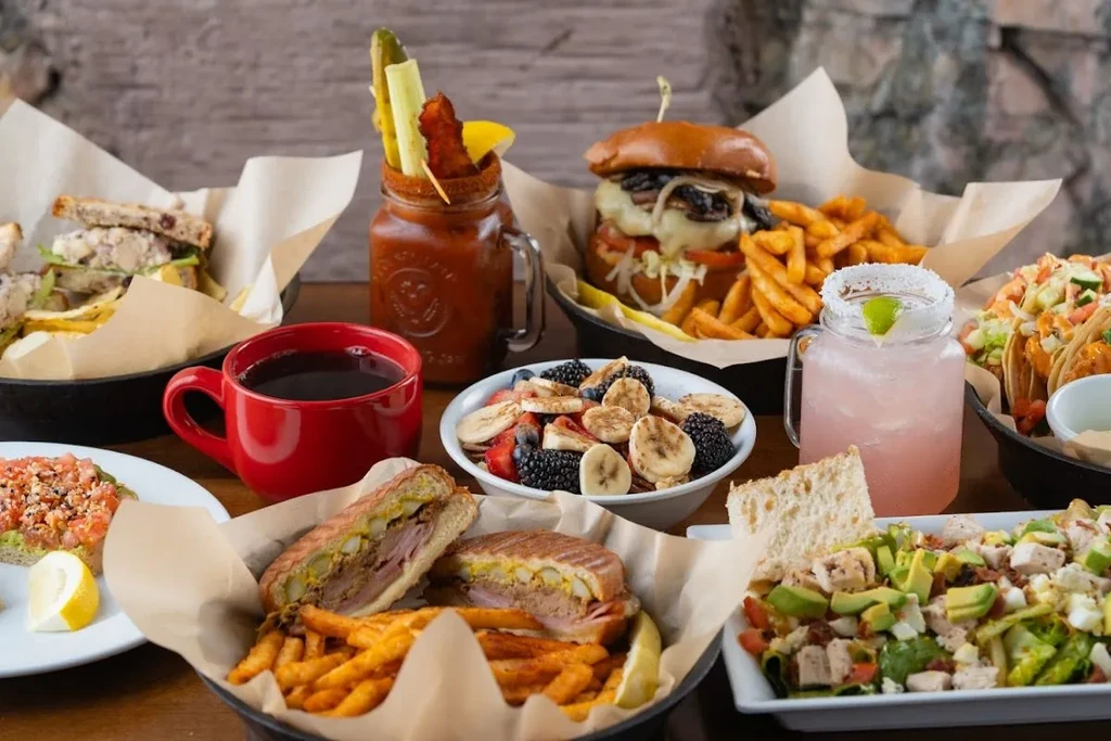 A large table spread with burgers, salads, fruit, coffee, and cocktails.