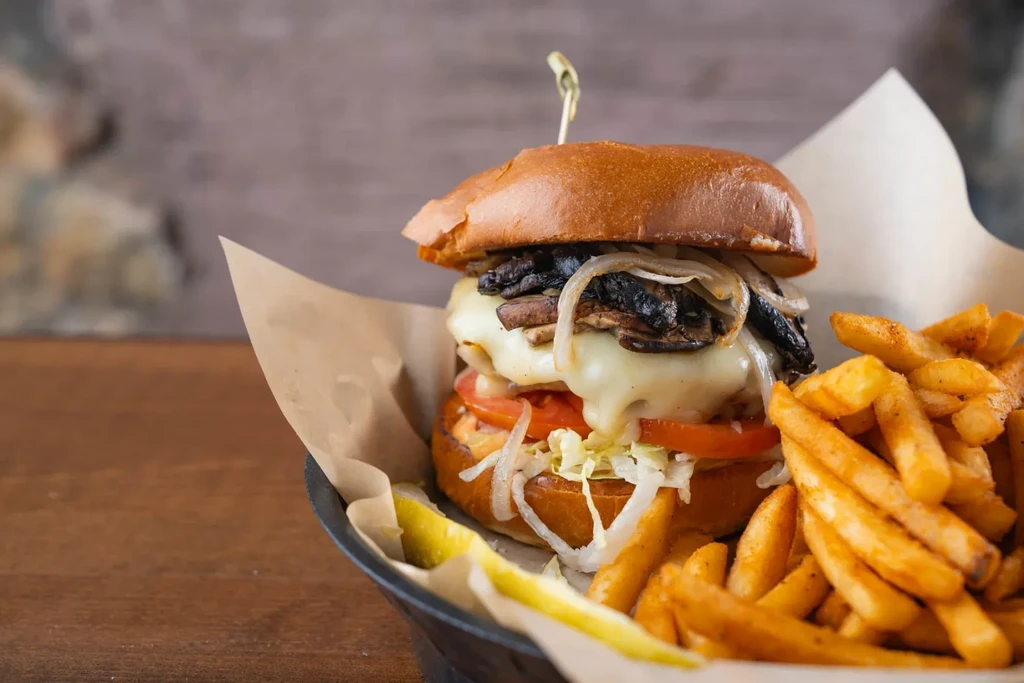 Stacked gourmet burger with melted cheese, mushrooms, and french fries.
