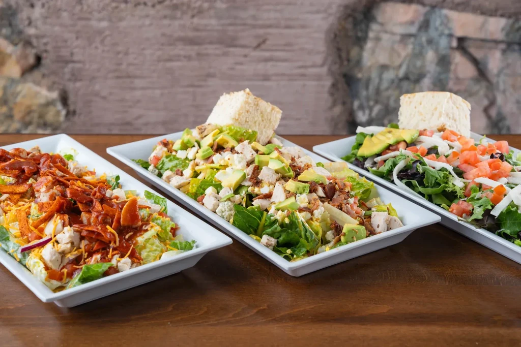 Three generous salads in white rectangular dishes on a rustic wooden table.