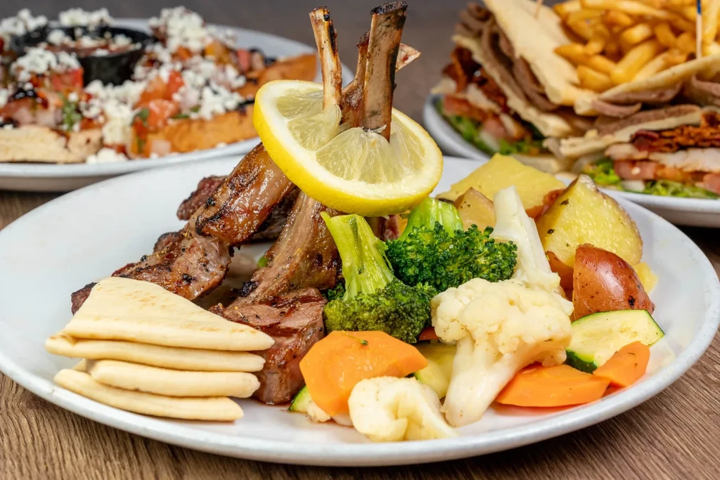 Grilled lamb chops, vegetables, and flatbread on a wooden table.