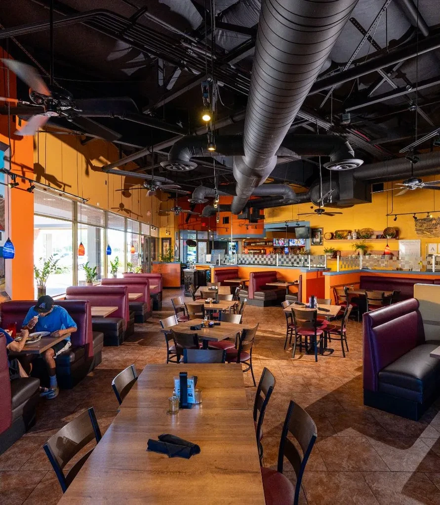 Modern casual restaurant interior with colorful walls, booths, and industrial ceiling.