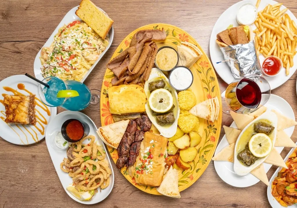 Overhead view of a large, diverse spread of Greek food and drinks.