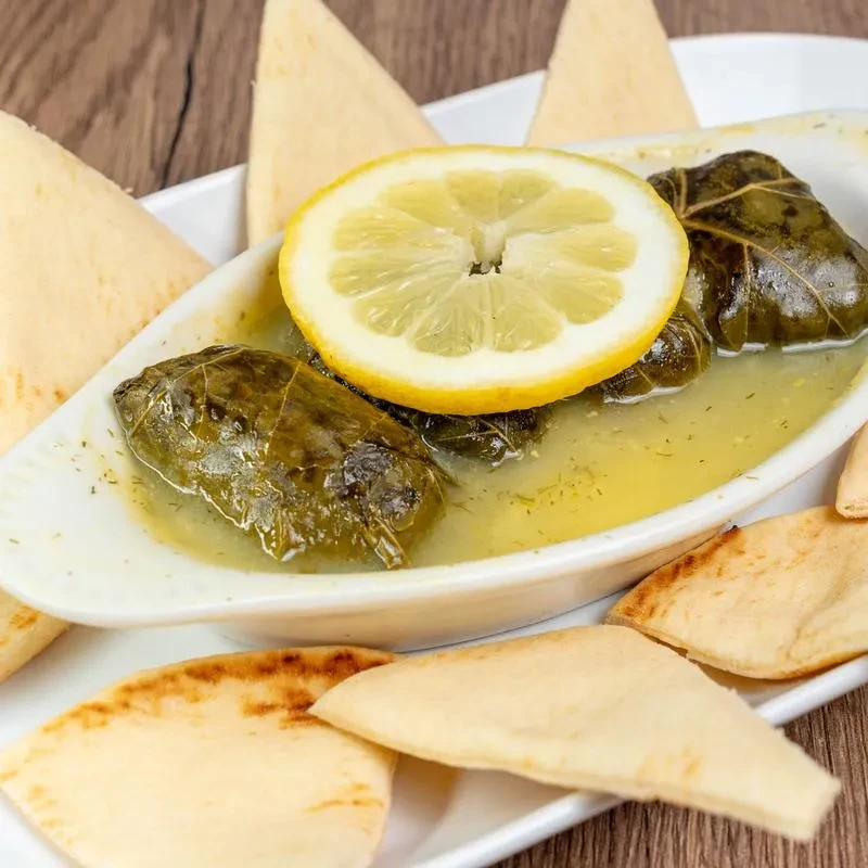 Stuffed grape leaves with lemon and pita bread on a wooden table.
