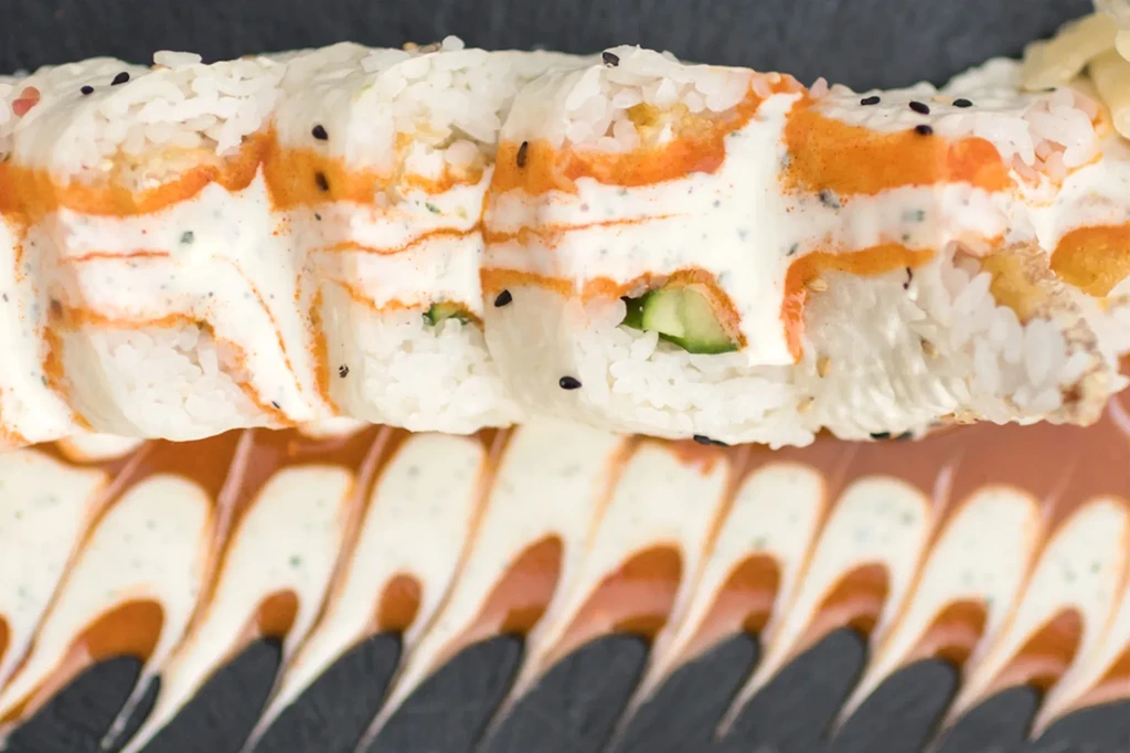 Maki sushi rolls drizzled with white and orange sauce and black sesame.
