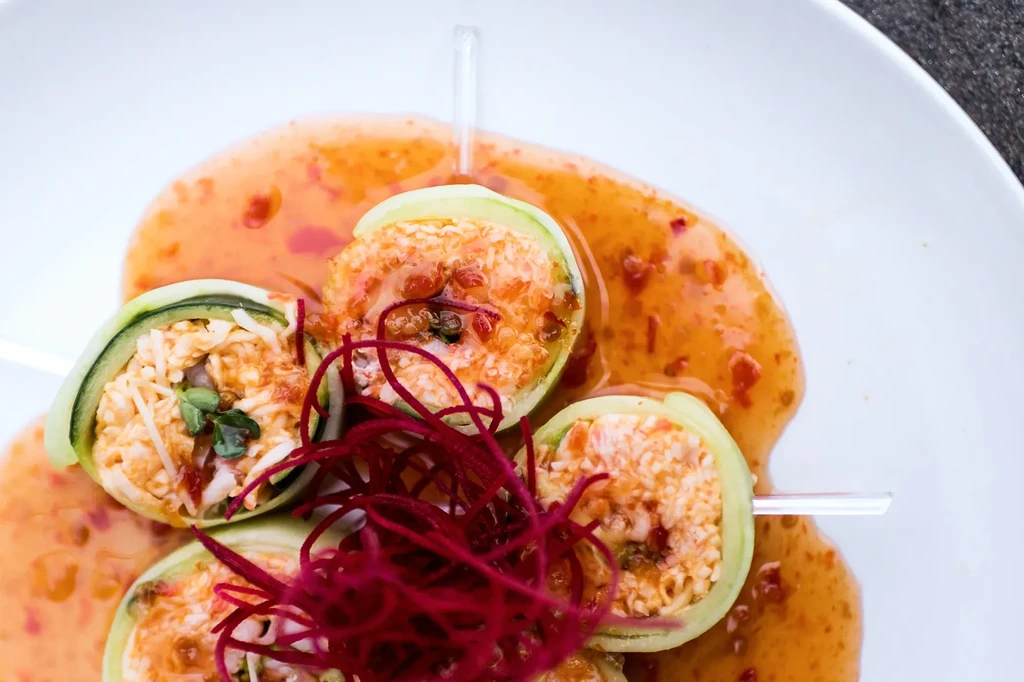 Four green vegetable rolls with creamy filling, red sauce, and sprouts.