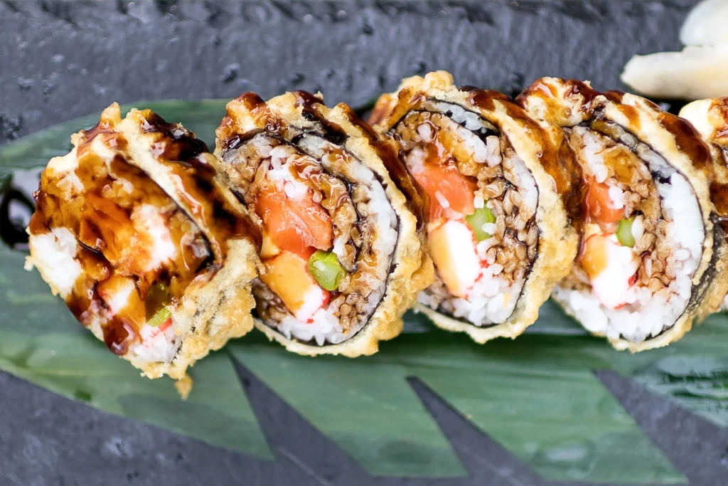 Crispy tempura sushi rolls, drizzled with dark sauce on a green leaf.