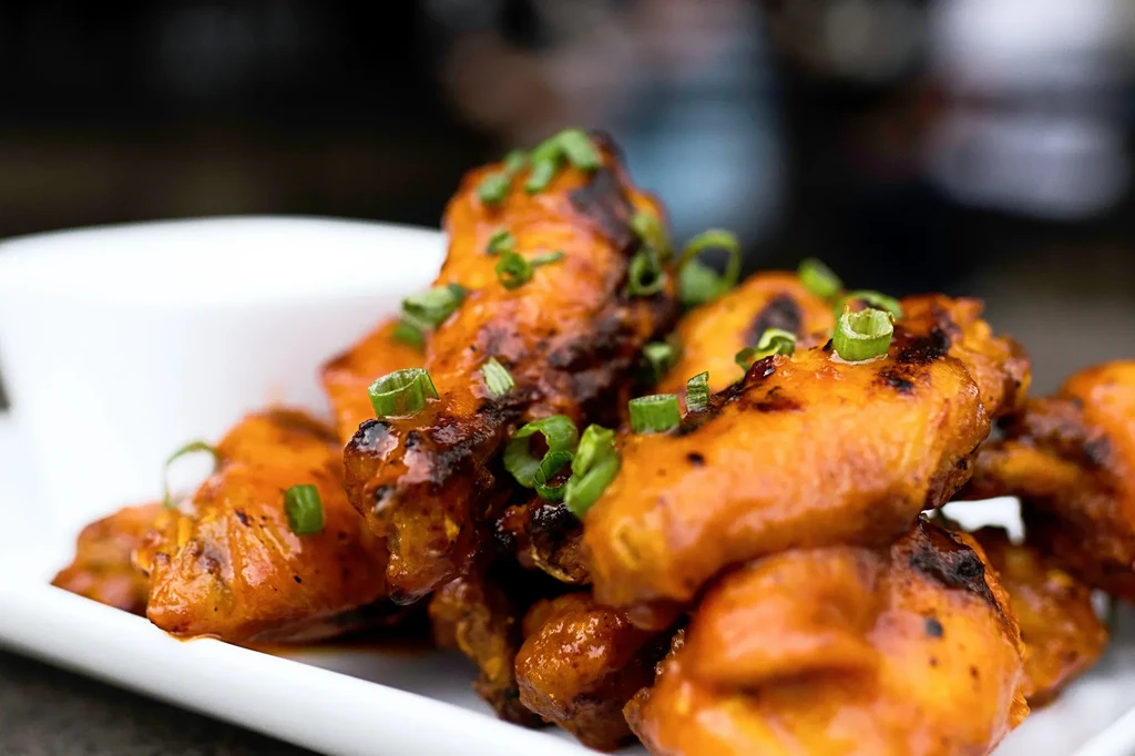 Glazed chicken wings topped with green onions on a white plate.