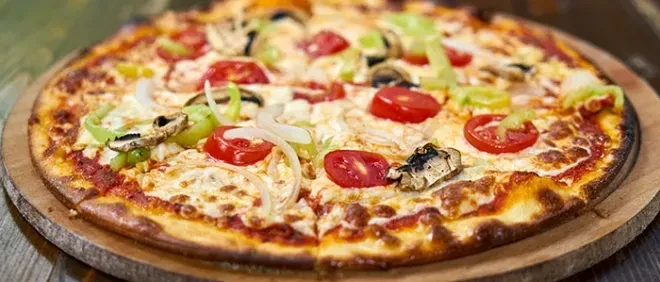 Whole pizza with mozzarella, vegetables, and mushrooms on a wooden board.