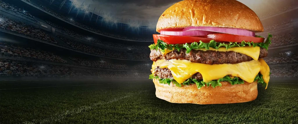 Stacked double cheeseburger with melted cheese, blurred night stadium.