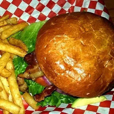 Overhead view of a hamburger with bacon, avocado, and french fries.