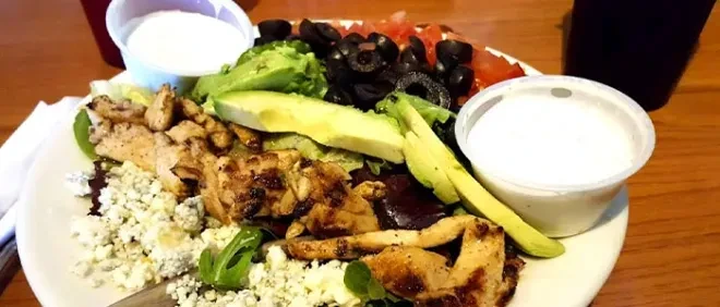 Large salad with chicken, avocado, blue cheese, tomatoes, olives, dressing.
