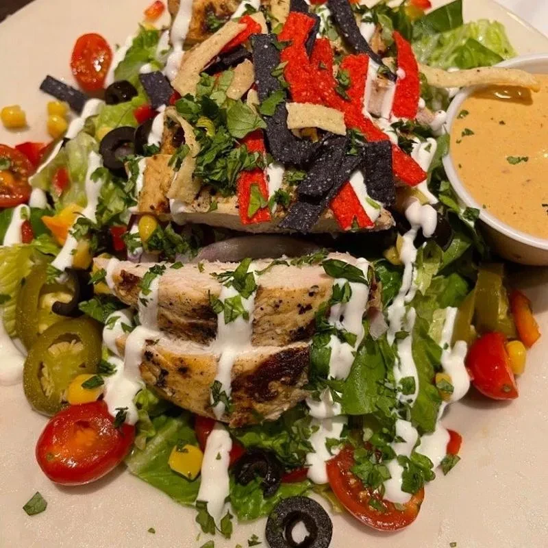 Grilled chicken salad with lettuce, vegetables, tortilla strips, and two dressings.