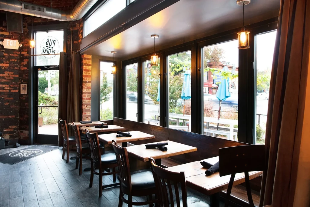 Warmly lit industrial-chic pub with wooden tables and street view.
