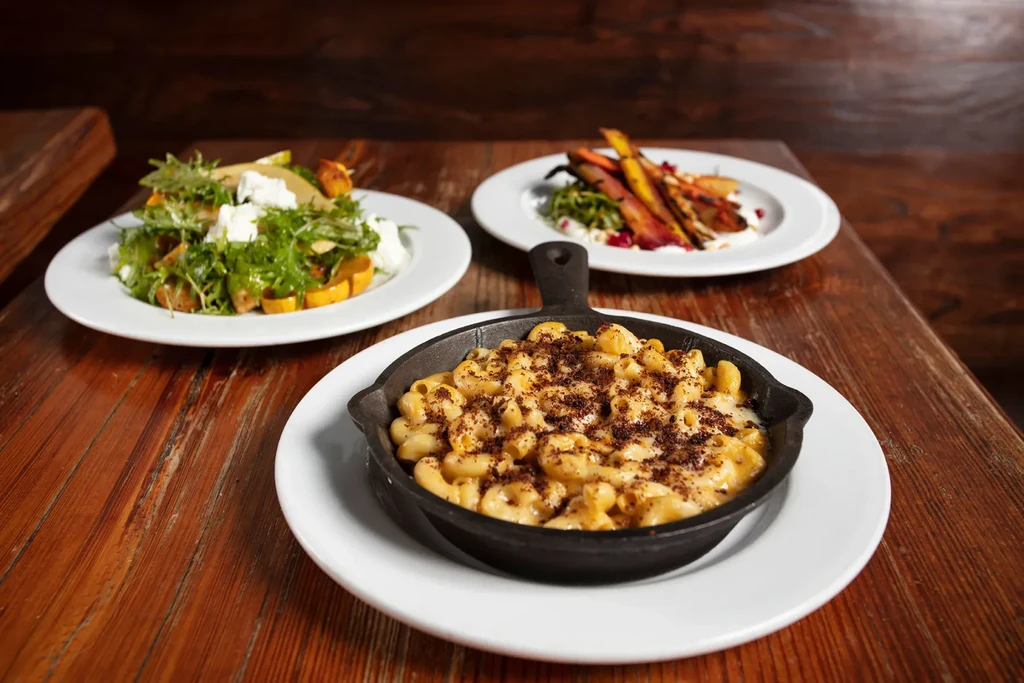 Skillet mac and cheese, a salad, and roasted carrots on a table.
