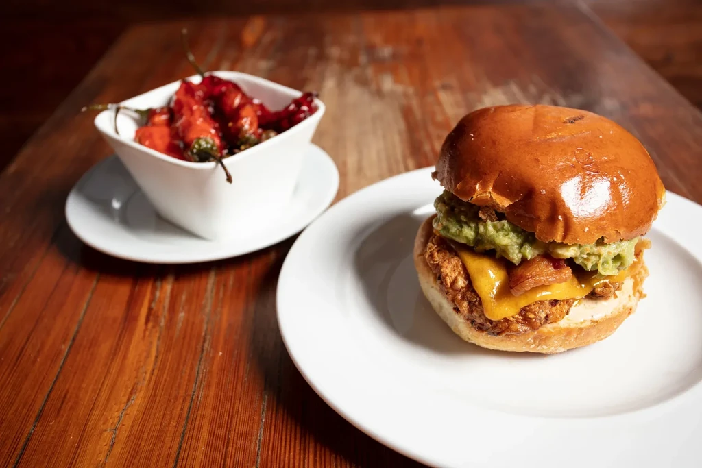 Gourmet burger with guacamole, melted cheese, and red peppers on wooden table.