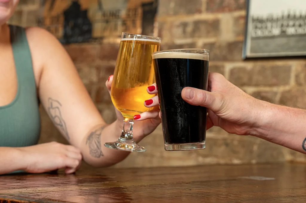 Close-up of two hands toasting with different types of beer.