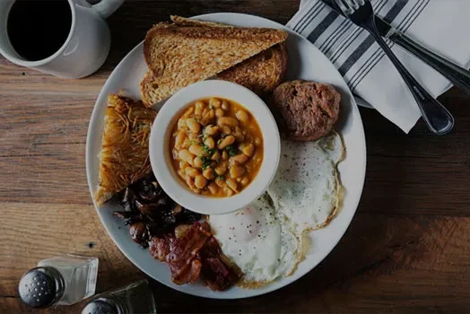 Full breakfast plate with eggs, bacon, toast, and coffee on wooden table.