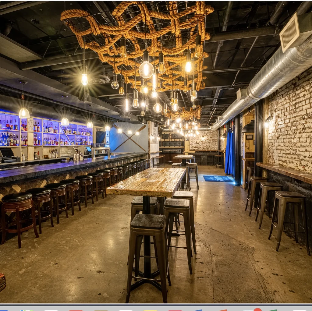 Industrial-rustic restaurant interior with dark bar, high tables, and unique rope lighting.