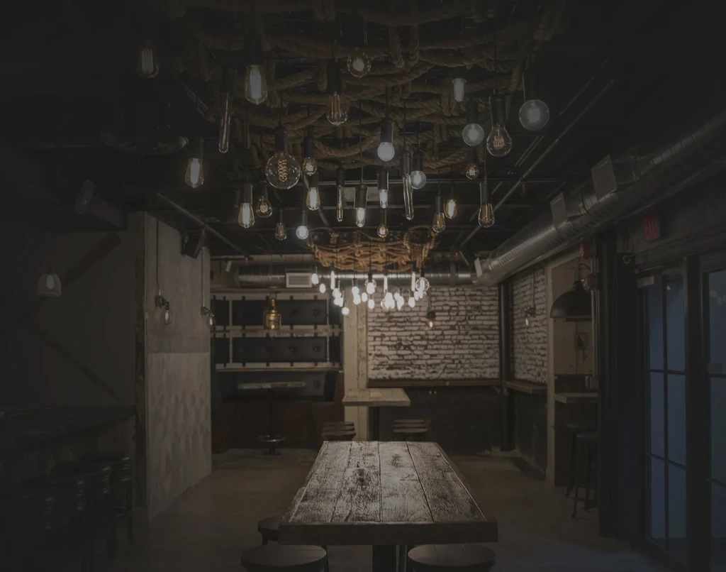 Dim industrial-chic restaurant interior, Edison bulbs, exposed ducts, wooden tables.