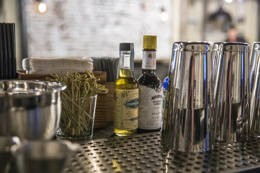 Close-up of a bar counter with cocktail tools, bitters, and shakers.