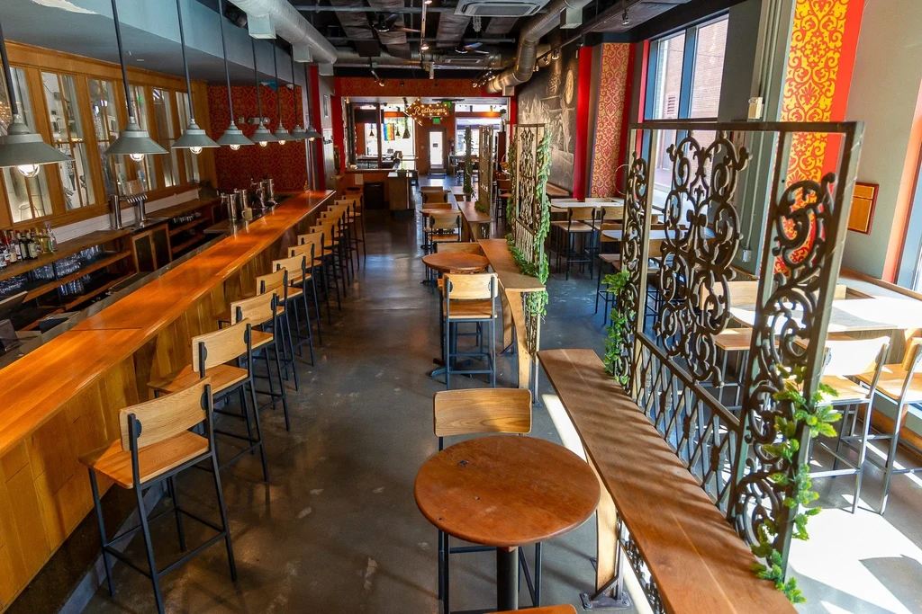 Empty modern industrial restaurant with bar, patterned walls, and green partitions.