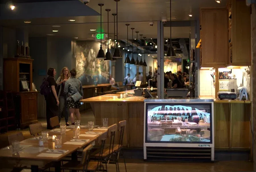 Rustic restaurant interior with a wooden bar, dining tables, and display case.