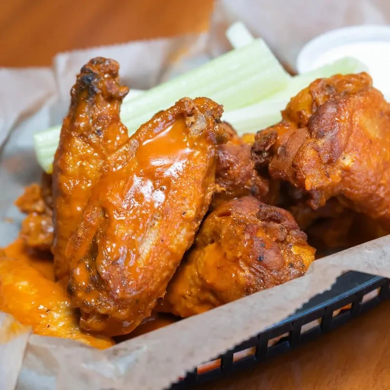Basket of Buffalo chicken wings with celery and dipping sauce.