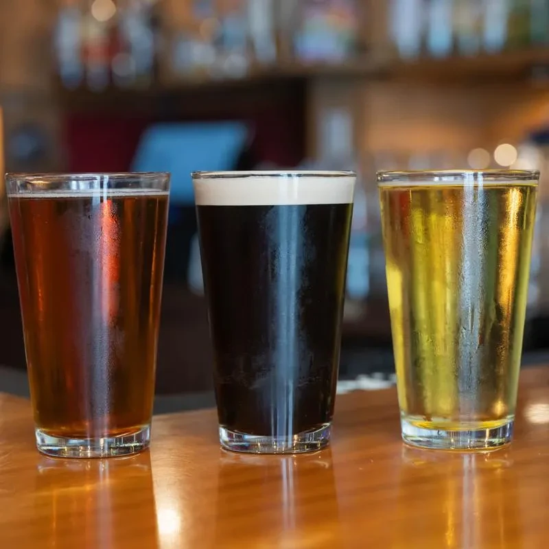 Three cold beers: amber, dark stout, and pale, on a wooden bar.
