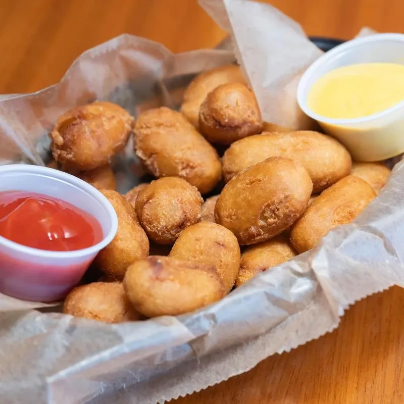Basket of crispy fried snacks, ketchup, and creamy yellow dipping sauce.