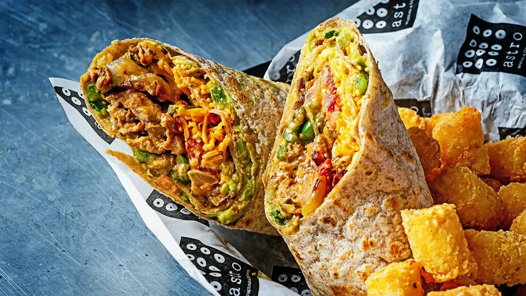 Halved burrito displaying meat, cheese, peppers, and crispy tater tots.