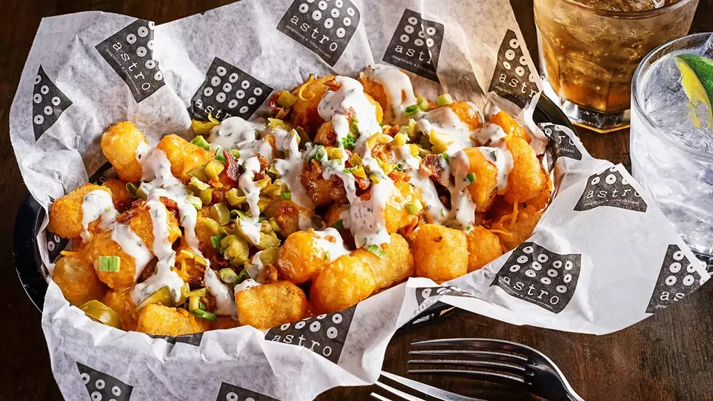 A basket of loaded tater tots with creamy sauce, bacon, and jalapeños.
