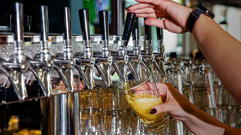 Close-up: Hands pour golden beer from a shiny tap at a bar.