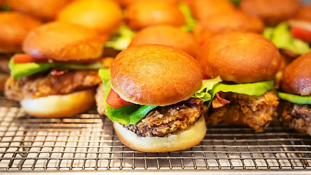 Close-up of many sliders with lettuce, tomato, and crispy patties.