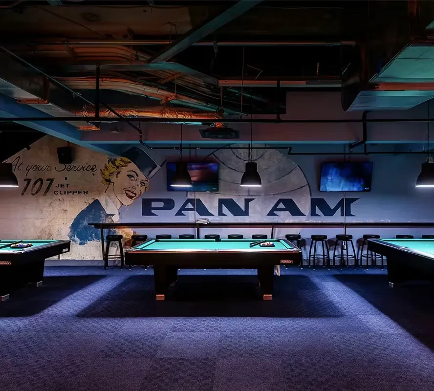 Retro bar with three pool tables and Pan Am themed murals.
