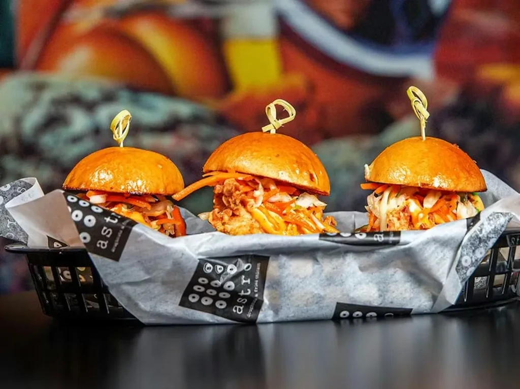 Three fried chicken and vegetable sliders in a basket.