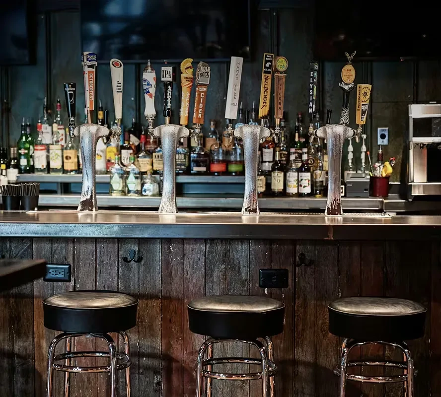 Empty bar with four beer taps, liquor bottles, and three bar stools.