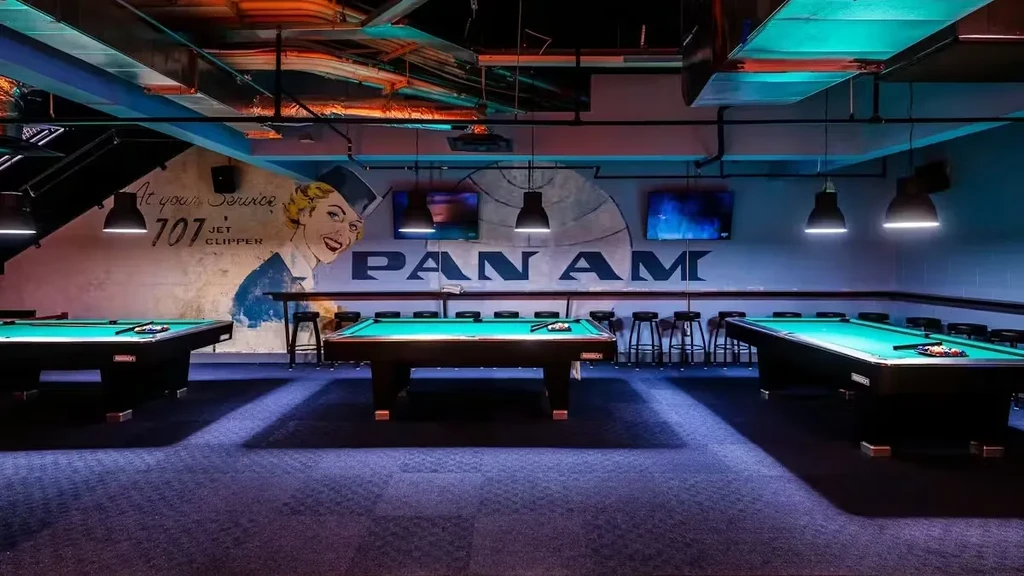 Three pool tables in a retro-industrial room with a Pan Am mural.