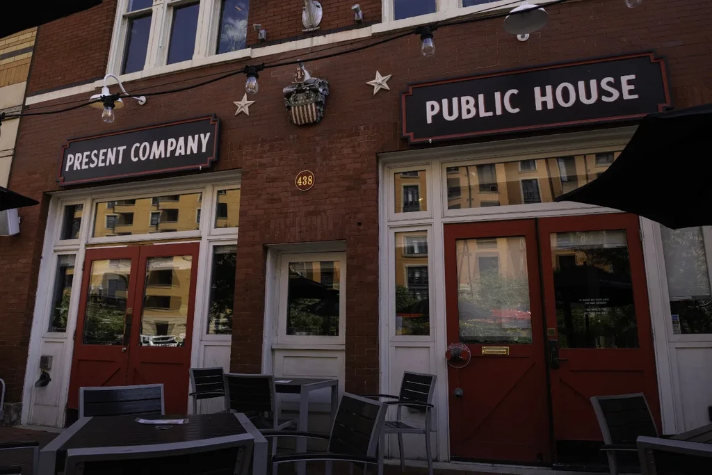 Present Company Public House: red-brick exterior, white windows, patio, string lights.