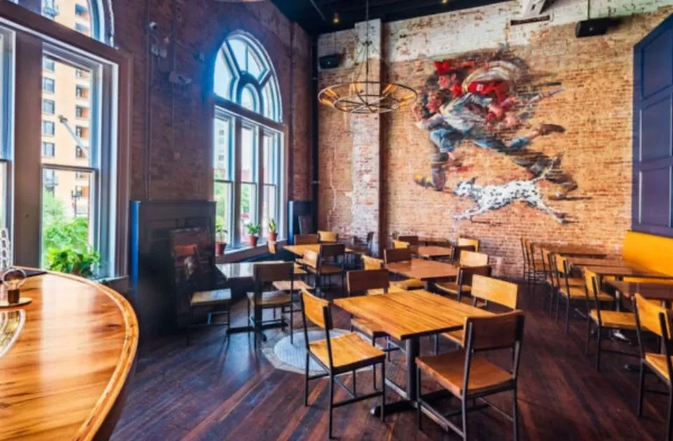 Industrial-chic restaurant interior with brick walls, colorful mural, wooden tables.