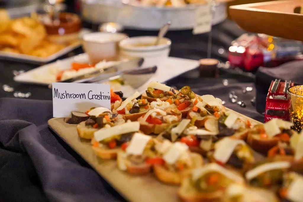 Labeled mushroom crostini with peppers and cheese on a buffet board.