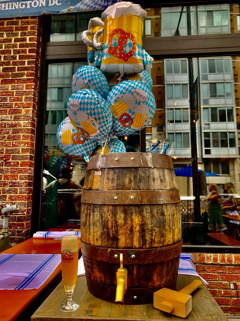 Wooden beer barrel with tap, glass of beer, and festive Oktoberfest balloons.