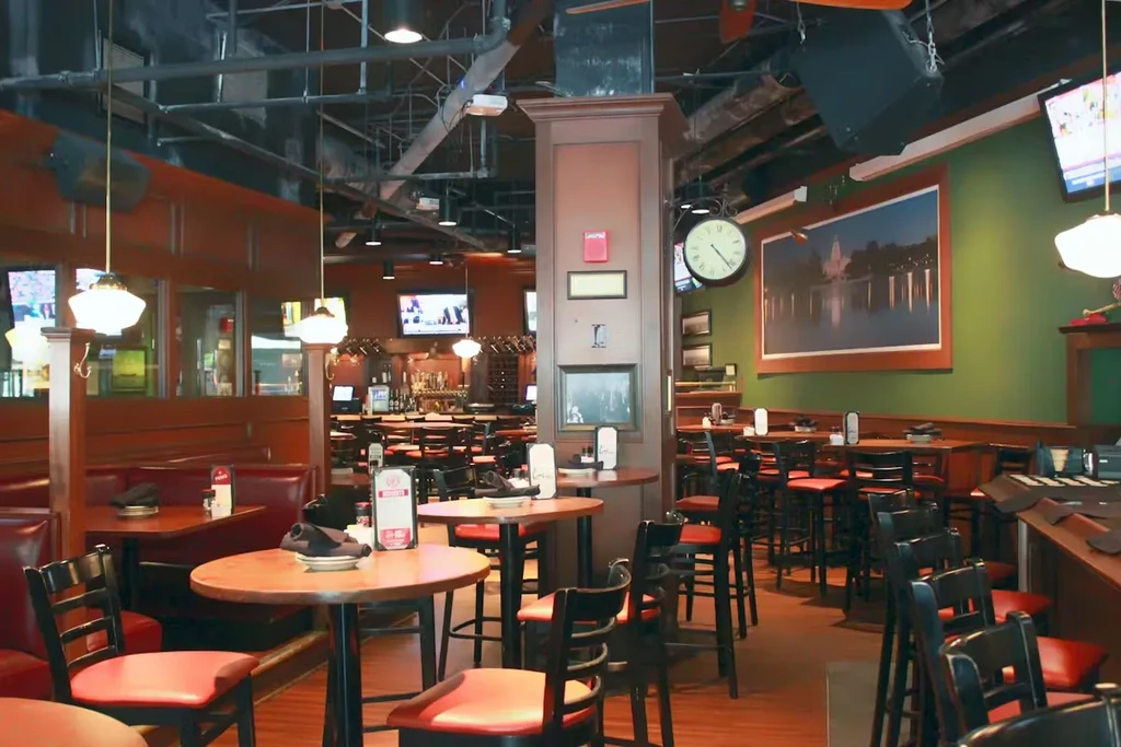 Casual restaurant interior with red booths, wood tables, exposed ceiling, and bar.