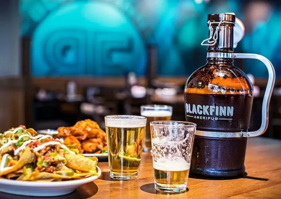 Cheesy nachos, Blackfinn Ameripub growler, and beers on a pub table.