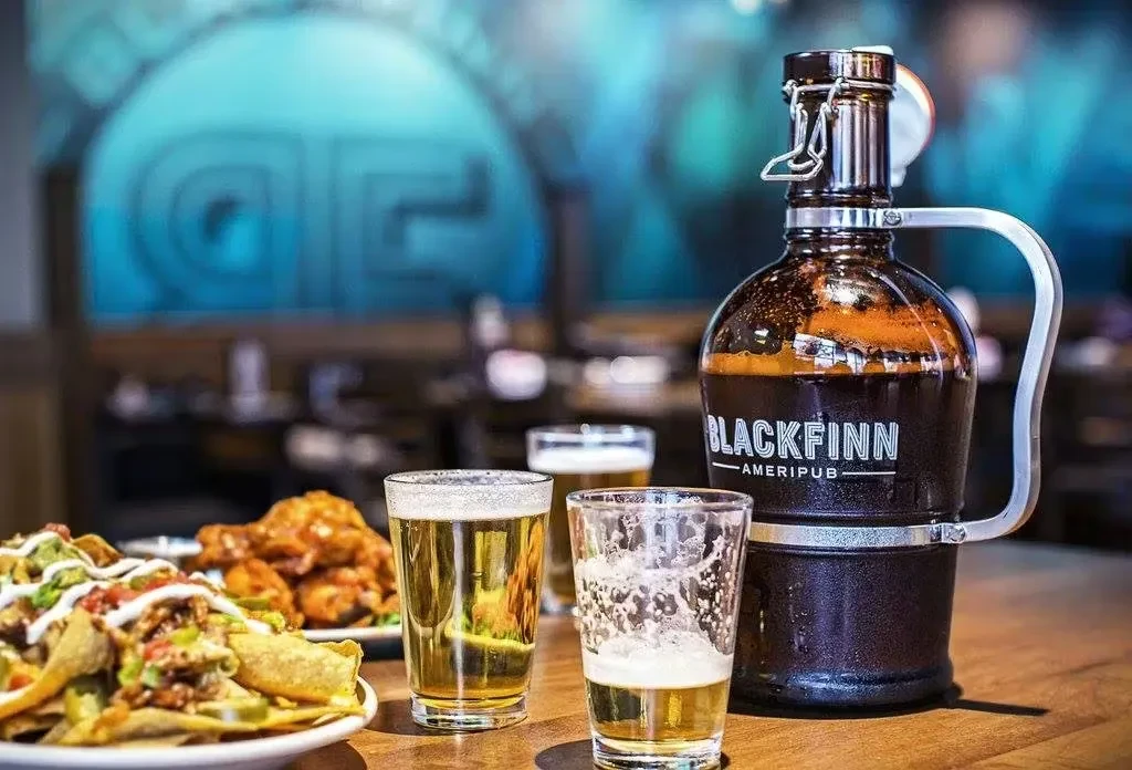 Piled nachos, two beers, and a Blackfinn Ameripub growler on a table.