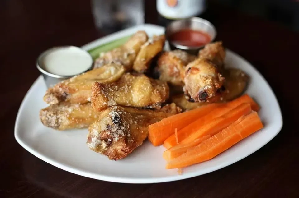 Crispy golden-brown chicken wings with carrot sticks and two dipping sauces.