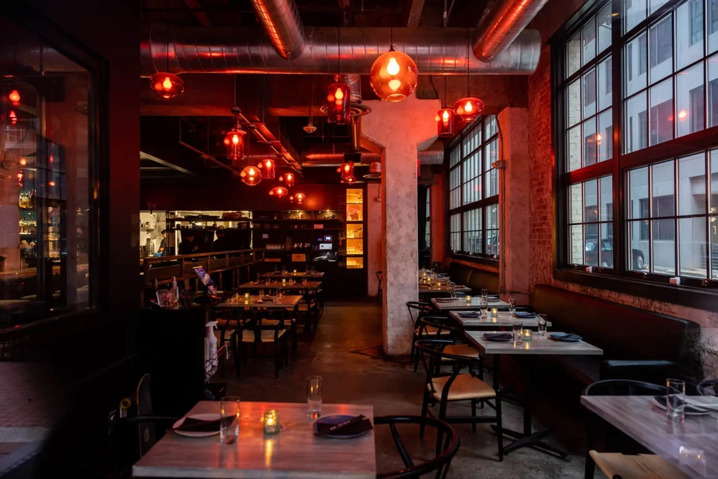 Warm red-orange lit industrial-chic restaurant interior with tables and booths.