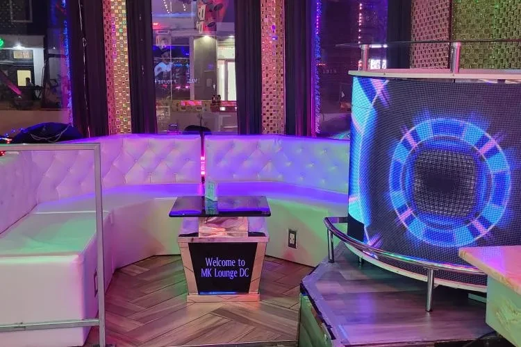 Vibrant lounge interior with white seating, 'MK Lounge DC' table, LED screen.